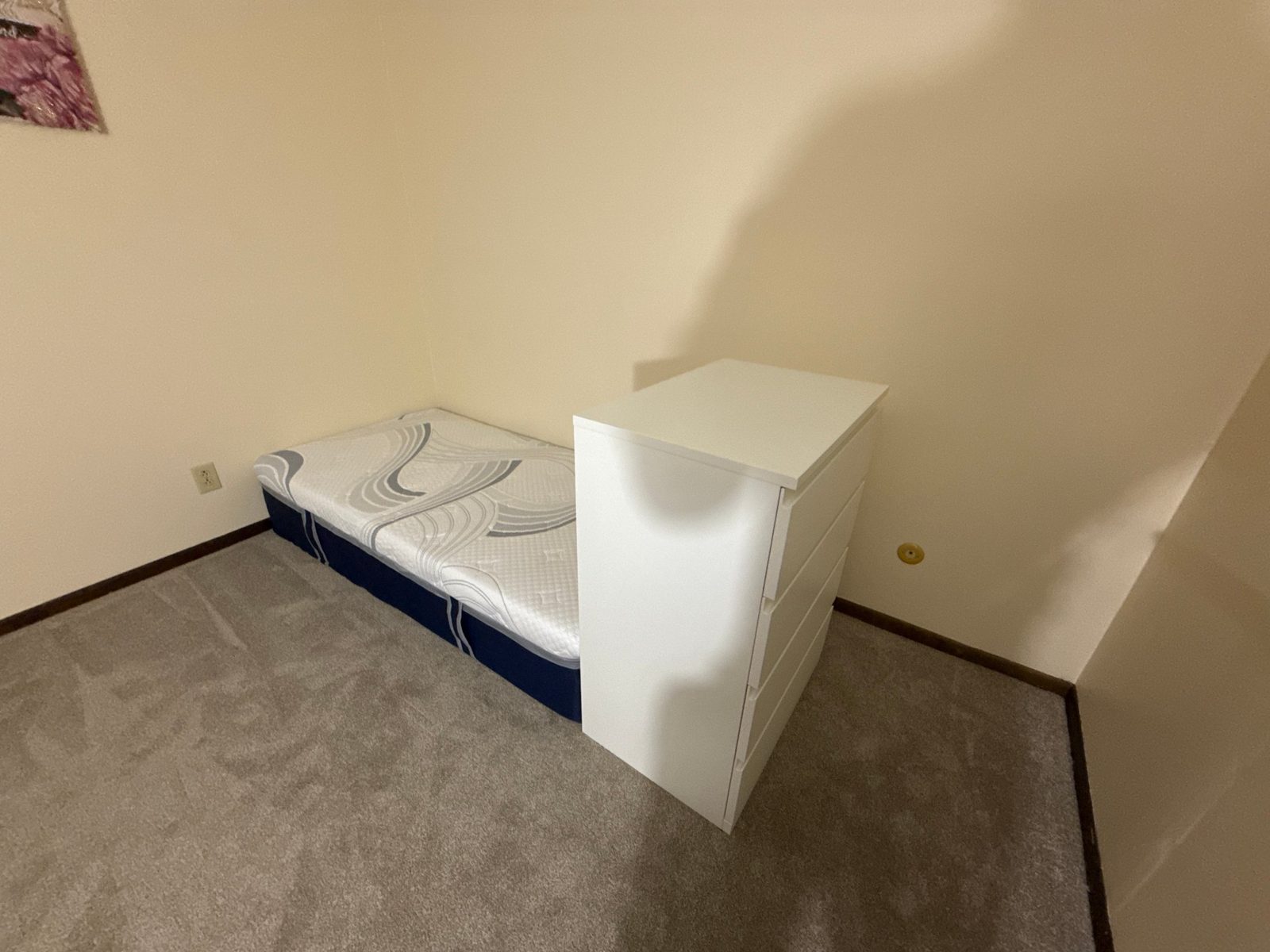 Bedroom corner before construction — mattress on the floor, dresser against the wall