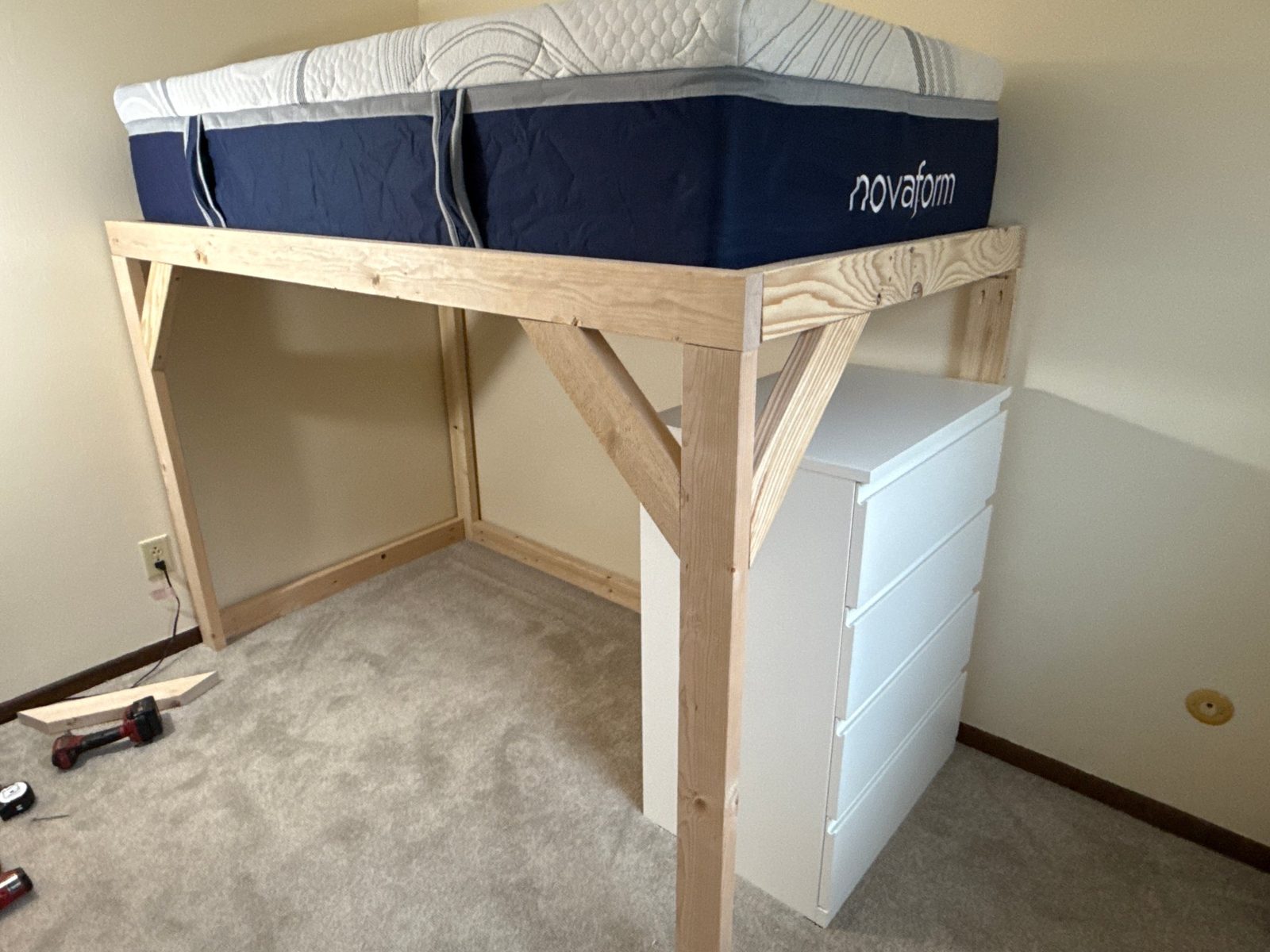Loft frame during construction — posts and knee braces carrying the deck, mattress test-fit on top, dresser fitted beneath