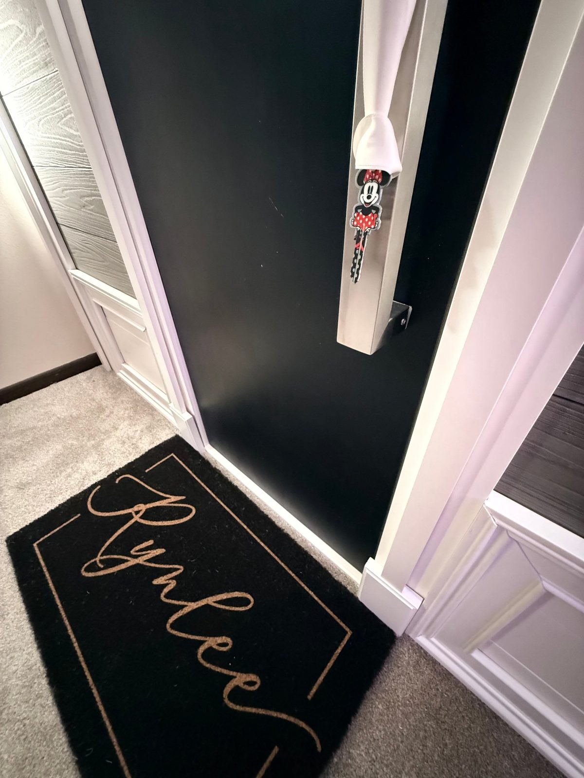 Close-up of the playhouse front door — black finish, metal pull with a ribbon, personalized doormat at the threshold