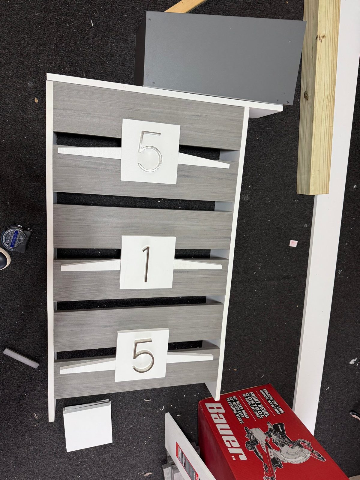 Mailbox post under construction on a workbench — horizontal composite slats with address numerals mounted, enclosure set above